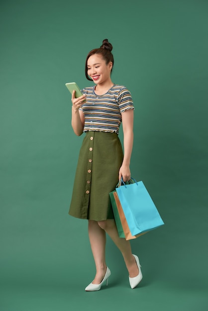 Cheerful elegant girl holding shopping bags while chatting on smartphone on green