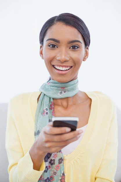 Cheerful elegant woman sitting on sofa text messaging