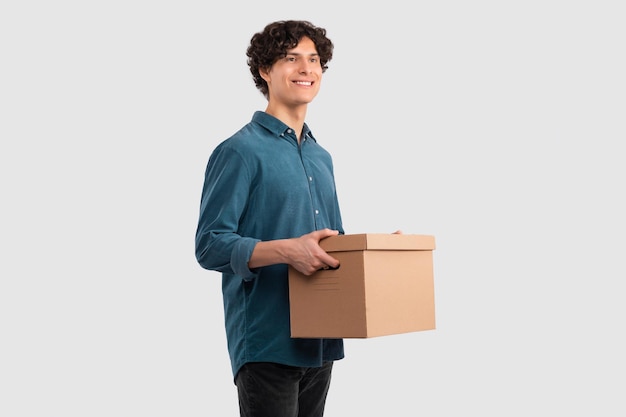 Cheerful european guy carrying cardboard moving box on white background