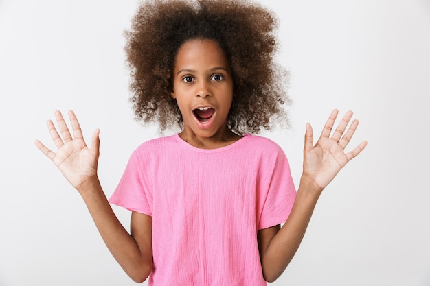 Cheerful excited little african girl wearing pink blouse standing isolated over white wall