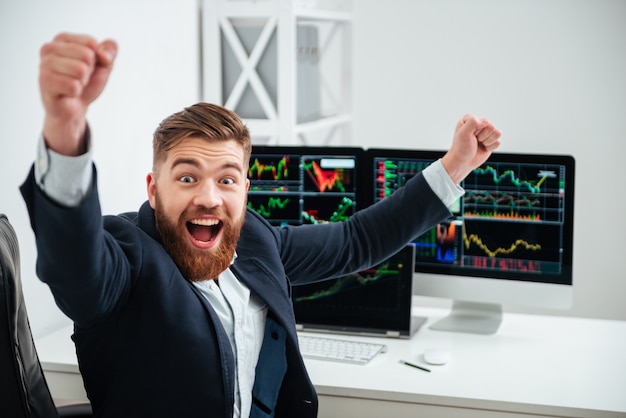 Фото Веселый возбужденный молодой бизнесмен с поднятыми руками кричит и празднует успех на рабочем месте в офисе