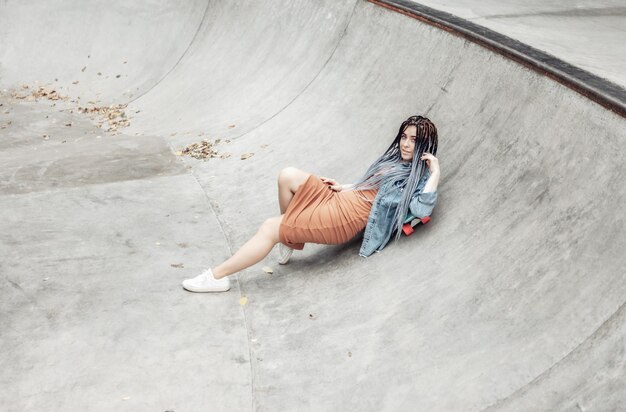 Cheerful extraordinary millennial woman with bright makeup and African lies on penny board in a skatepark