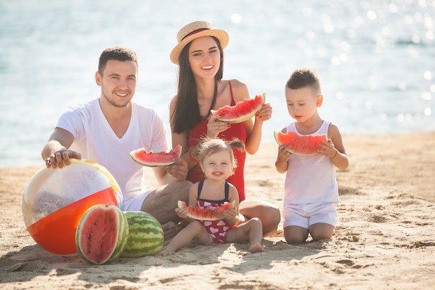 Famiglia allegra che mangia anguria sulla spiaggia. i bambini piccoli ei loro genitori in riva al mare si divertono. famiglia allegra in riva al mare