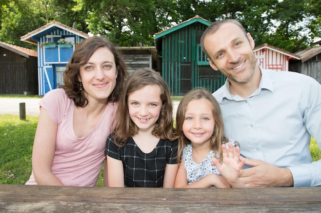 Cheerful family of four sit on wood table on park in summer spring day