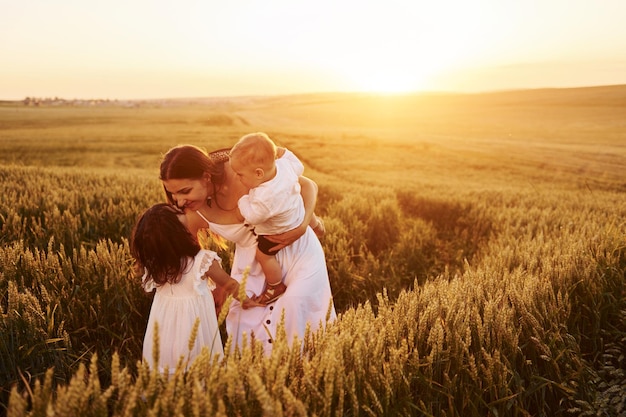 Cheerful family of mother little son and daughter spending free time on the field at sunny day time of summer