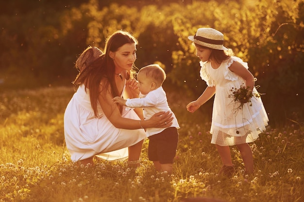 Cheerful family of mother little son and daughter spending free time on the field at sunny day time of summer