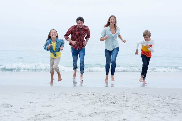 Famiglia allegra che funziona alla spiaggia contro il cielo