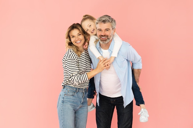 Cheerful family of three embracing standing over pink background