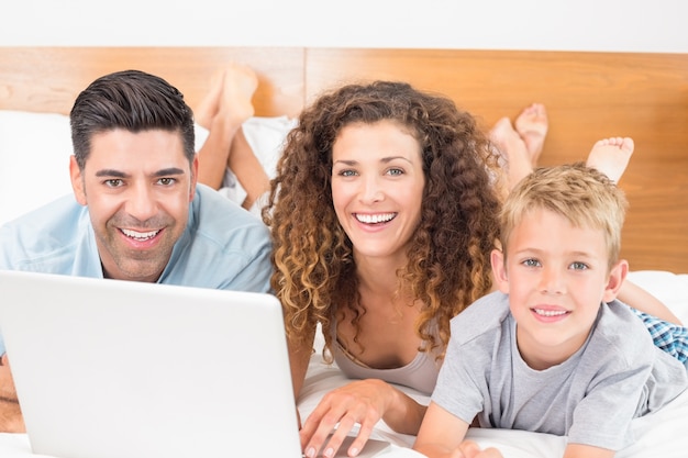 Cheerful family using laptop together on bed