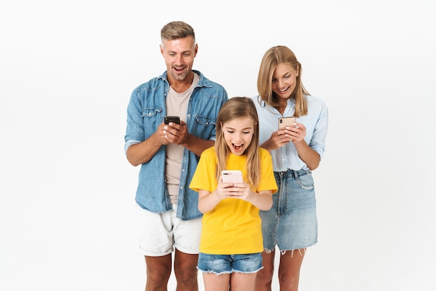 Cheerful family wearing casual outfit standing isolated on white, looking at mobile phones