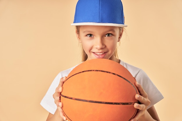 ゲームボールを保持し、明るいオレンジ色の背景に立って笑っている陽気な女性の子バスケットボール選手