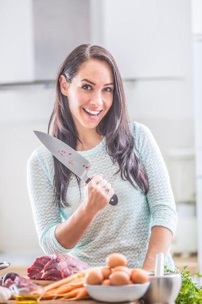 Cheerful female cook in kitchen with joy and sharp knife preparing lunch.