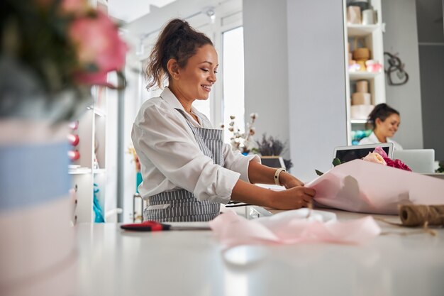 Cheerful female florist completing floral composition with decorative paper