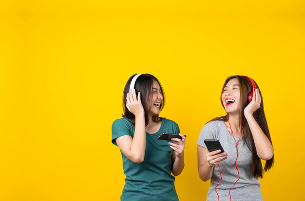 Cheerful female friends listening music against yellow background