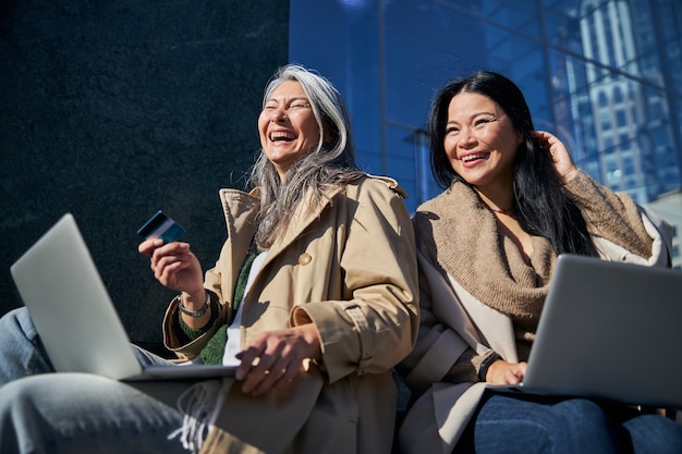 Cheerful female friends using laptops for online shopping