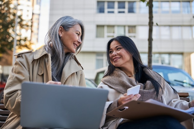 Cheerful female friends using modern gadgets on the street