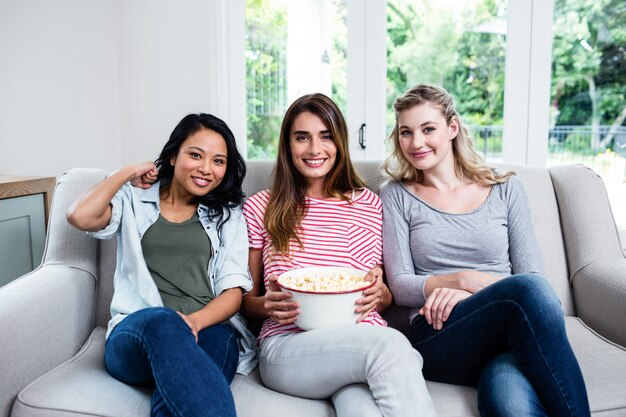 Cheerful female friends with popcorn sitting on sofa