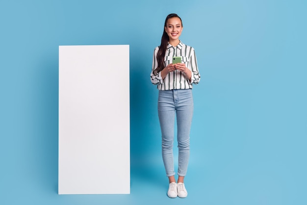 Cheerful female holding big cellphone blank screen advertising application over blue studio background