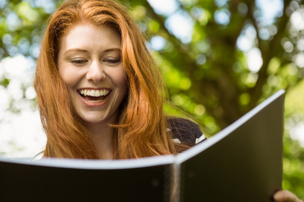 Photo cheerful female student reading book in park