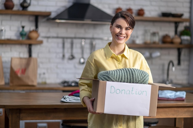 Cheerful female volunteer demonstrating a cardboard box full of clothes