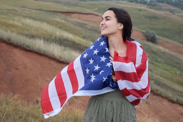 cheerful female wraps in usa flag standing on hill