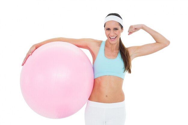 Cheerful fit woman flexing muscles with fitness ball