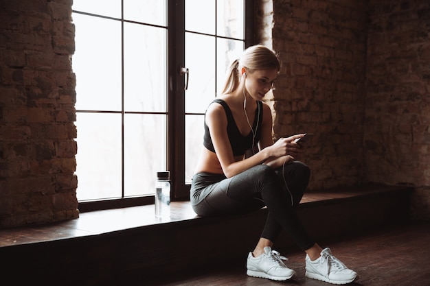 Cheerful fitness woman using phone and listening music