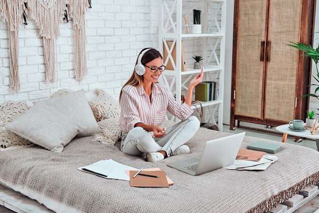 Cheerful freelancer in headset gesturing near laptop in bedroom Woman have videocall