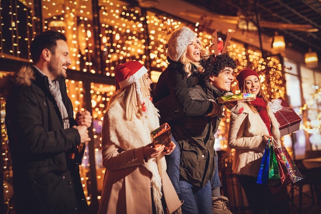 Cheerful friends having fun in city mall in christmas night, with bright shop window in background