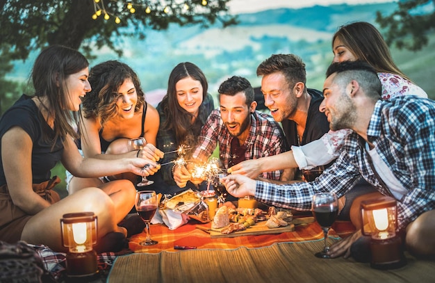 Cheerful friends holding sparklers on field during picnic