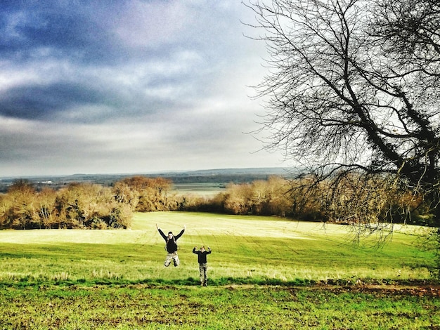 Photo cheerful friends jumping over field against sky