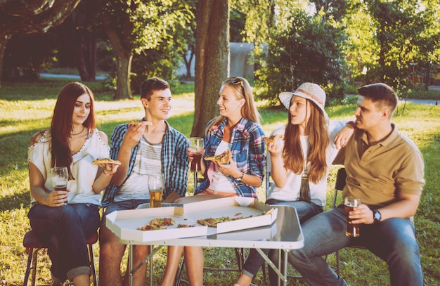 Cheerful friends on picnic in the park. Eating pizza