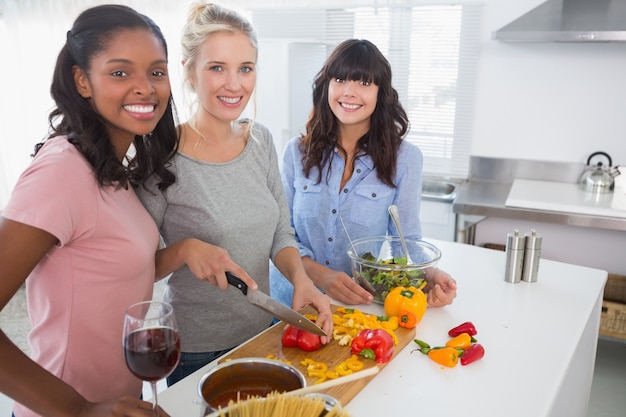 Cheerful friends preparing a meal together looking at camera