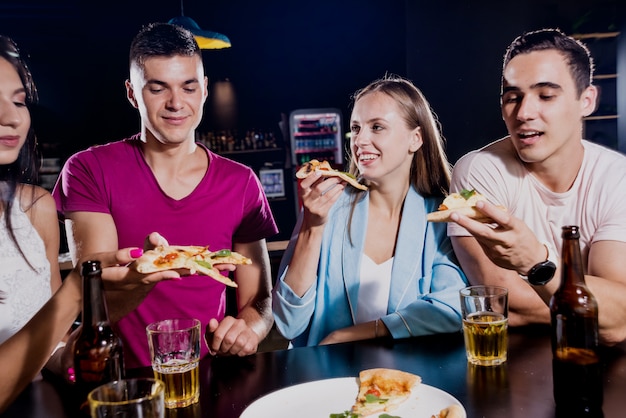 Cheerful friends in the pub. Drinking beer, eating pizza, talking, having fun.