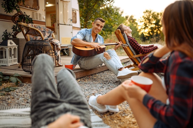 Photo cheerful friends sing songs with guitar on picnic at camping in the forest