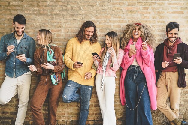 Cheerful friends smoking while using mobile phone against wall