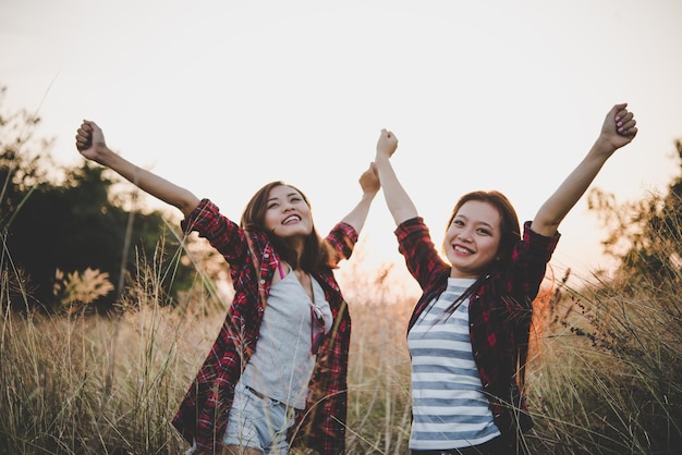 Photo cheerful friends with arms raised standing on grassy field