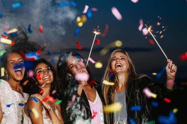 cheerful friends with multi colored confetti falling at beach during dusk