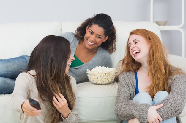 Cheerful friends with remote control and popcorn bowl at home