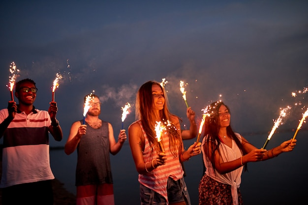 Веселые друзья с бенгальскими огнями на летнем пляже