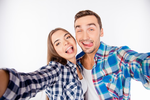 Cheerful funny couple in love making selfie photo showing tongue