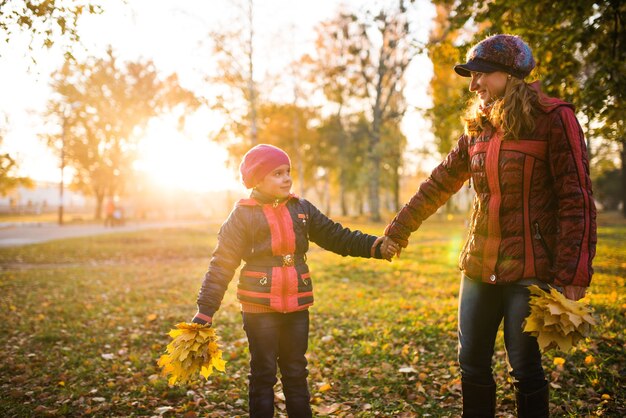 Cheerful and funny mother plays with her positive daughter yellow maple leaves