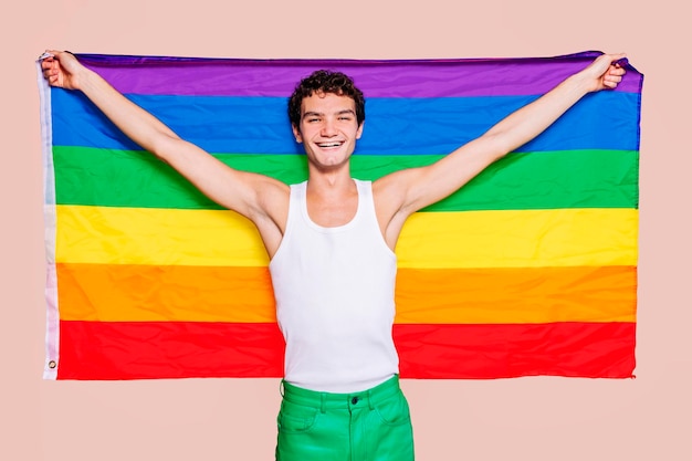 スタジオで虹色の旗を保持している陽気なゲイの少年