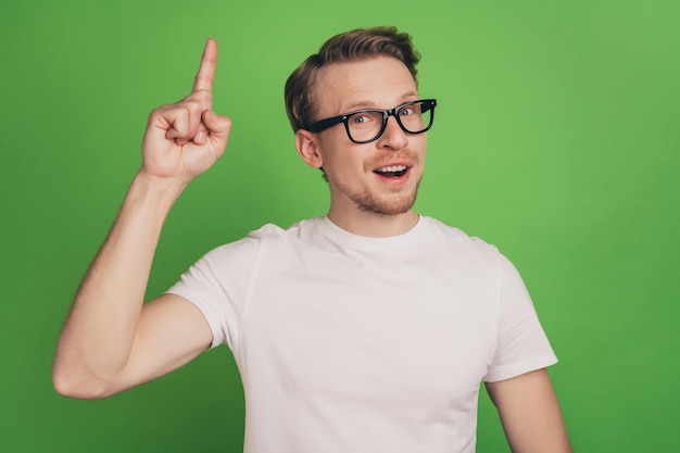 L'uomo allegro genio nerd freelancer alza il dito ha idea di indossare occhiali isolati su sfondo di colore verde