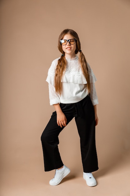 Cheerful girl 12 years old holds her hair and poses. Children's fashionable outfit.