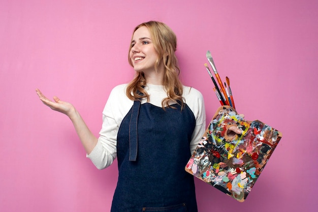 Cheerful girl artist holds gear for drawing and shows with her hand a place for text