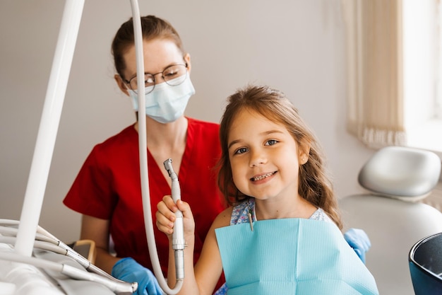 Cheerful girl child holding dental drill and smiling in dentistry The child smiles at the consultation with the dentist