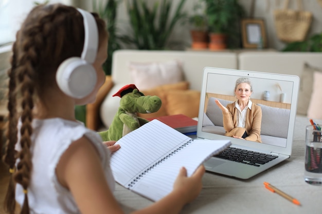 Foto ragazza allegra in cuffia che usa il computer portatile che studia tramite il sistema di e-learning online