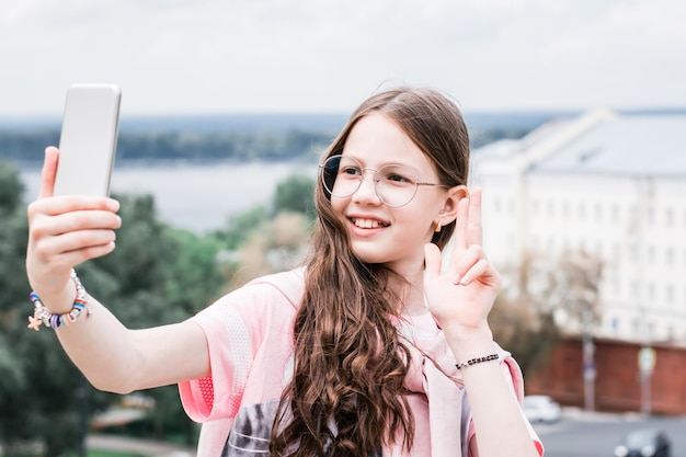A cheerful girl in glasses takes a selfie on a smartphone Content for social networks