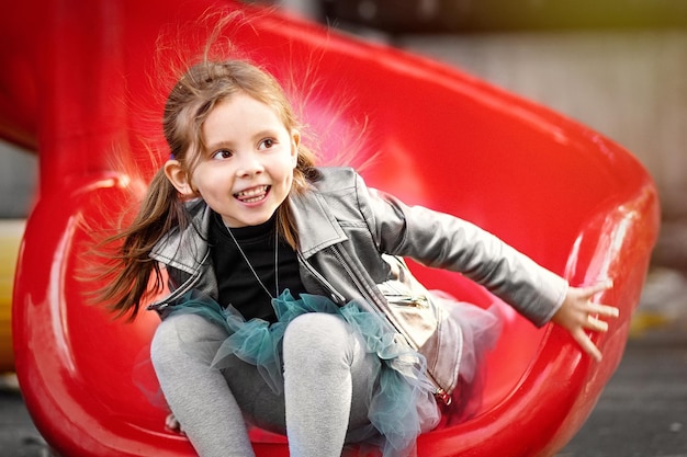 A cheerful girl is riding a playground slide and laughing Emotional outdoor portrait of a child